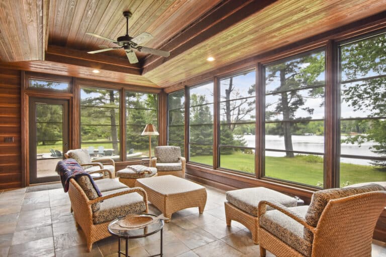 A sunroom with wicker furniture and a view of the lake.