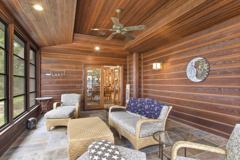A screened in porch with wicker furniture and a ceiling fan.